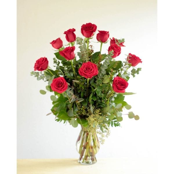Dozen Roses arranged in vase with mixed greenery.